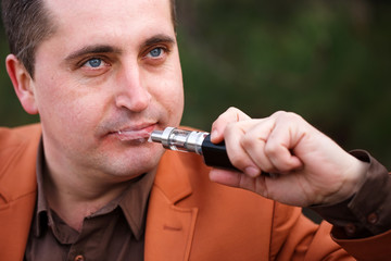 A young man sits on a bench and smokes an electronic cigarette.