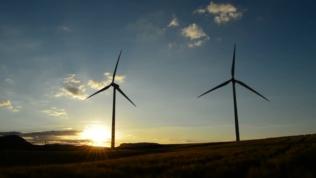 Wind turbine rotating in field at sunset at cloudy day