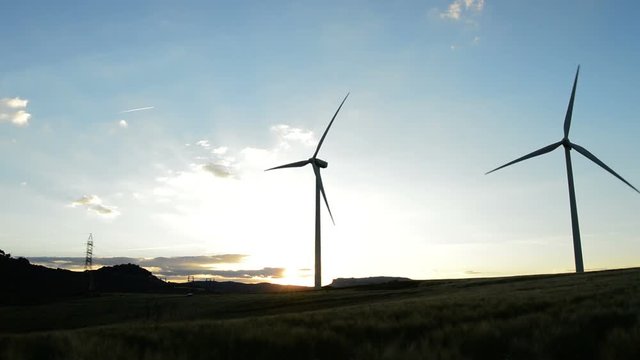 Wind turbines energy at field moving at sunset