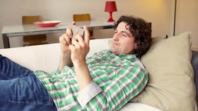 Man texting on smartphone and receiving bad news while lying on the sofa

