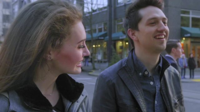 On a city street, a cute couple smile and laugh together