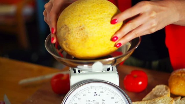 Woman checking weight of melon on scales in kitchen
