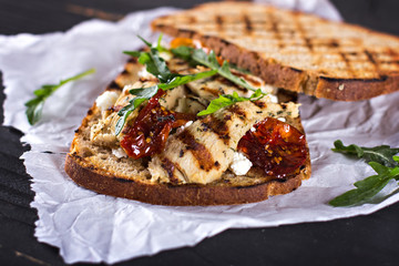 Sandwich with grilled chicken, sun-dried tomatoes, cheese and rocket salad on a wooden table