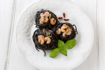 Plate of black spaghetti with prawn on white table
