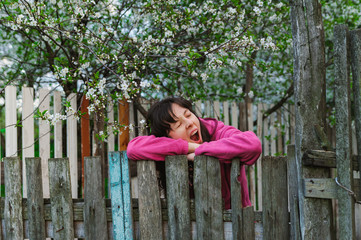 young woman standing by old fence and yawn