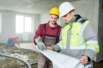 foreman builder and construction worker with blueprint in indoor apartment