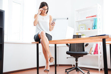 Businesswoman sitting on the table and using smartphone