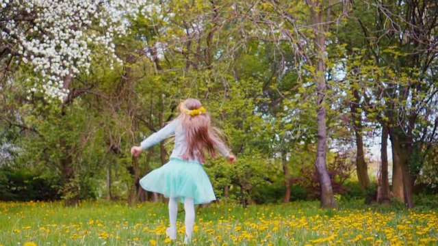 Cute girl 7-8 years old with blond long hair with wreath of dandelions on the head running and spinning in the park