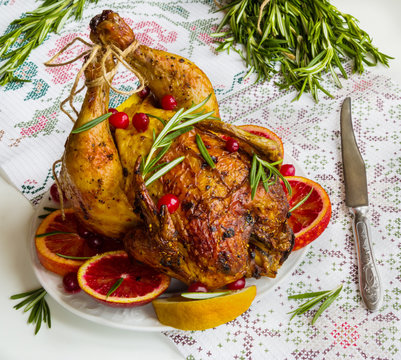 Roasted whole chicken on white table. Served with red oranges, lemon, rosemary and cranberries.