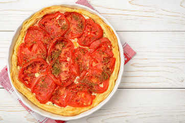 Quiche with creme cheese and tomatoes on white wooden table.