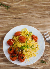 Pasta with small cherry tomatoes baked with garlic, salt and olive oil. White plate on wooden background. Top view.