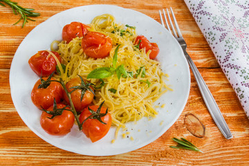 Pasta with small cherry tomatoes baked with garlic, salt and olive oil. White plate on wooden background.