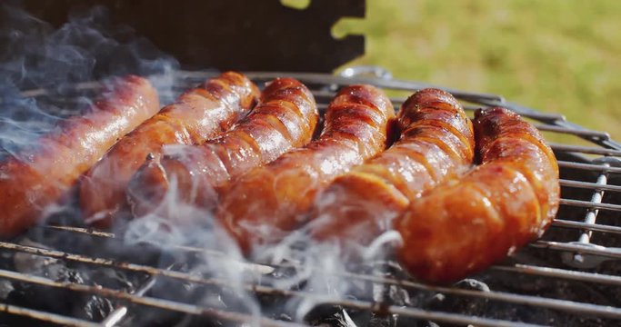 Thick juicy sausages grilling on a fire in an outdoor portable barbecue on a green lawn in the garden