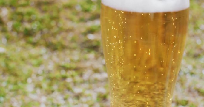 Close up on the mid section of a glass of refreshing ice cold beer or lager with a frothy top served outdoors in the garden on a summer picnic.