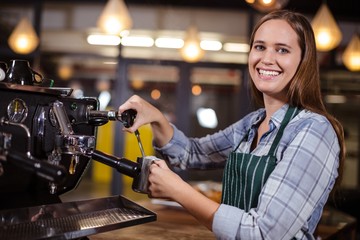 Fototapeta na wymiar Smiling barista making hot milk with coffee machine