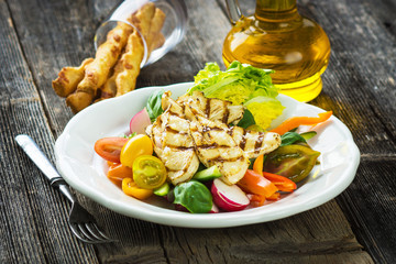 Delicious salad with grilled chicken breast on a wooden background