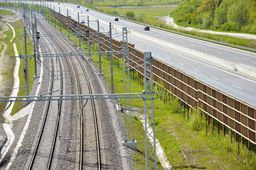 Modern railway route and highway separated by fence in countryside