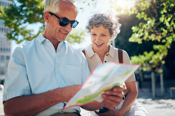Elderly couple sitting outdoors on a bench and using city map
