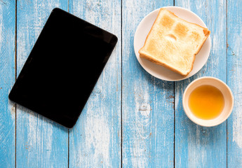 Black display Tablet , Toast, Honey on blue wooden floor.