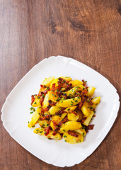 fried potatoes with bacon in a plate on wooden table