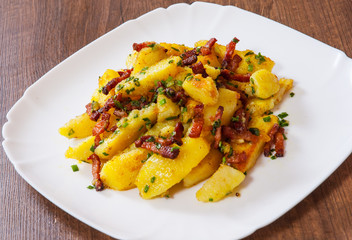 fried potatoes with bacon in a plate on wooden table