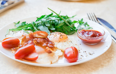 Breakfast on plate - fried eggs, fried bacon, cherry tomatoes, ruccola, black ground pepper and red sauce