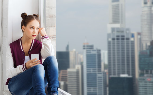 teenage girl sitting on windowsill with smartphone