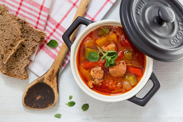 Gulasch in einer schwarzen cocotte mit Majoran auf weißem Holz
