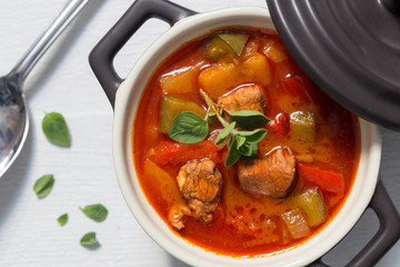 Gulasch in einer schwarzen cocotte mit Majoran auf weißem Holz