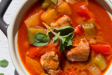 Gulasch in einer schwarzen cocotte mit Majoran auf weißem Holz