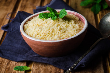 Couscous in clay bowl on wooden background. Selective focus. Toned image
