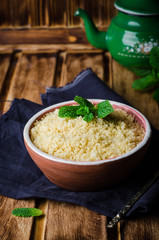 Couscous in clay bowl on wooden background. Selective focus. Toned image