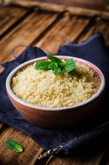 Boiled couscous in clay bowl on wooden background. Selective focus