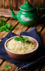 Boiled couscous in clay bowl on wooden background. Selective focus