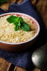 Boiled couscous in clay bowl on wooden background. Selective focus