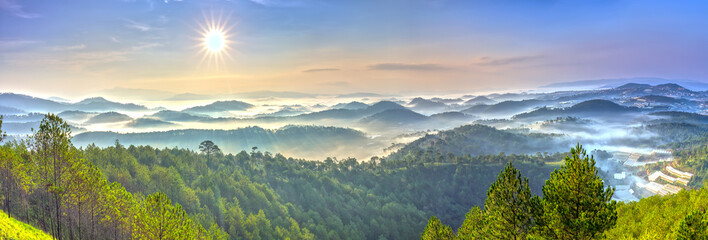 Naklejka premium Panorama sunrise over hill with the sun radiating golden rays pierced the hills with pine trees covered with morning dew beautiful ray beam forming to welcome the new day so simple in Dalat, Vietnam