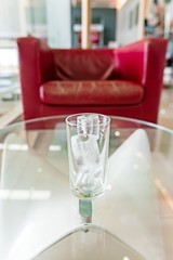 glass with ice cubes on a glass table and blurry red sofa background
