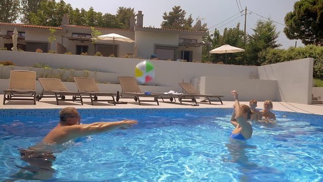 Slow motion of a mother and grandfather playing volleyball in the outdoor pool while boy and grandmother watching them. Happy summer time at vacation home
