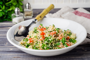 Couscous salad with parsley and tomatoes on wooden background. Selective focus. Eastern cuisine