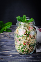 Couscous salad with parsley in jar and tomatoes on dark  wooden background. Selective focus. Eastern cuisine