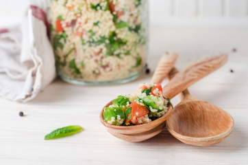 Couscous salad with parsley and tomatoes in jar  on white wooden background. Selective focus. Eastern cuisine
