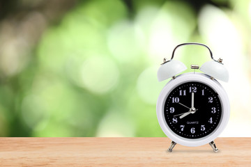 white classic alarm clock on wood table have blurred green leaf nature in background