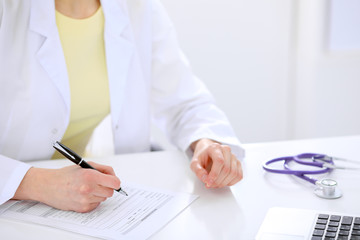 Close-up of a female doctor filling  out application form , sitting at the table in the hospital