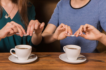 Hands of two women putting sugar in a cup of coffee