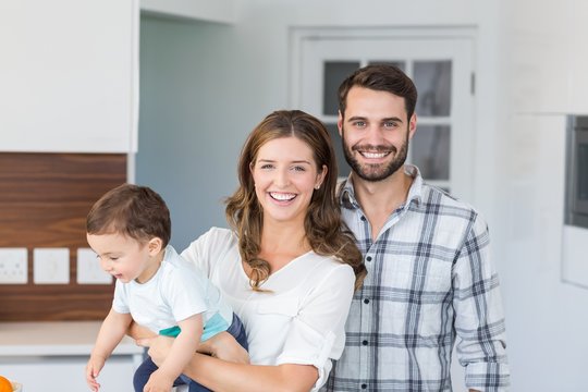 Happy Couple With Baby Boy Standing In Living Room