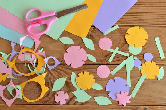 Paper flowers, paper sheets, scissors, paper scrap on a wooden table. Paper flower craft for kids. Children's art project. 