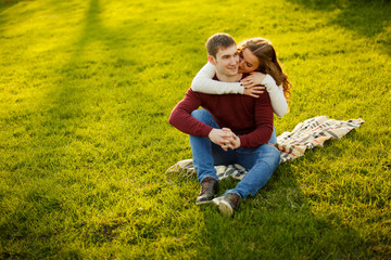 Fototapeta premium Young couple spend a weekend or holiday in park or pine forest. Against backdrop of mist or fog. Family values, spending time together, youth. Hug and kiss each other on grass. Solid sweaters