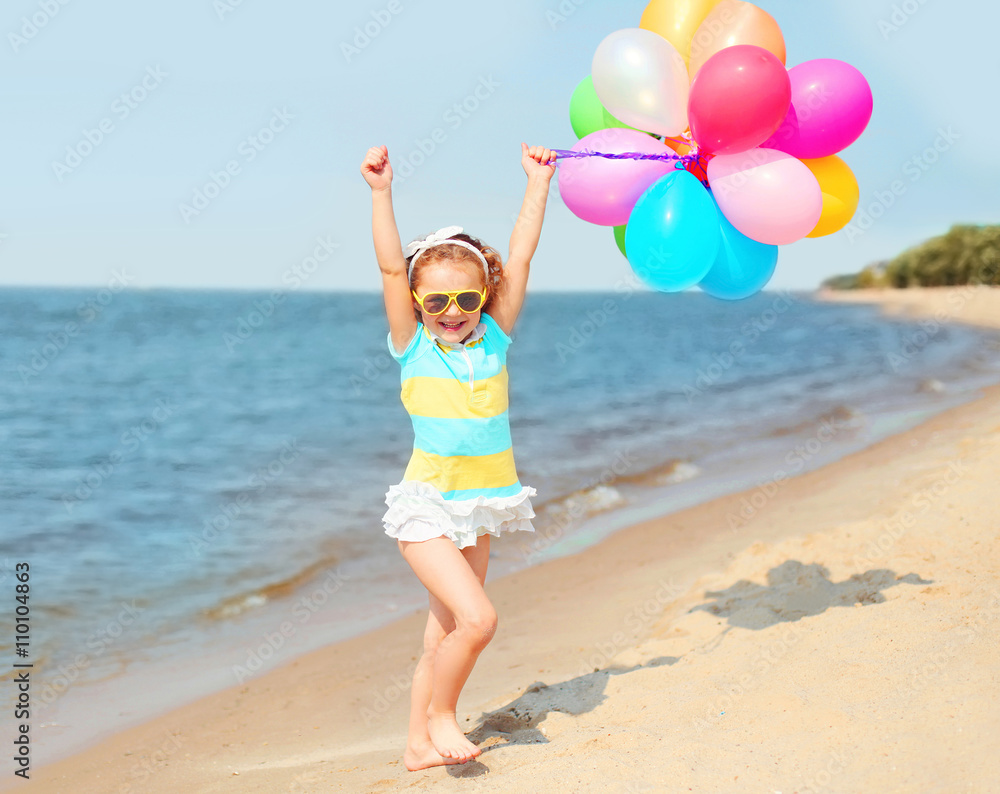 Wall mural Happy smiling child on beach playing with colorful balloons near