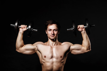 Handsome athletic man with dumbbells confidently looking forward. Strong bodybuilder with six pack, perfect abs, shoulders, biceps, triceps and chest. Great fitness body. Ideal for commercial 