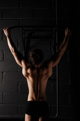 Fototapeta na wymiar Athlete muscular fitness male model pulling up on horizontal bar. Sporty and healthy muscular man. Perfect fitness body. Ideal for commercial.